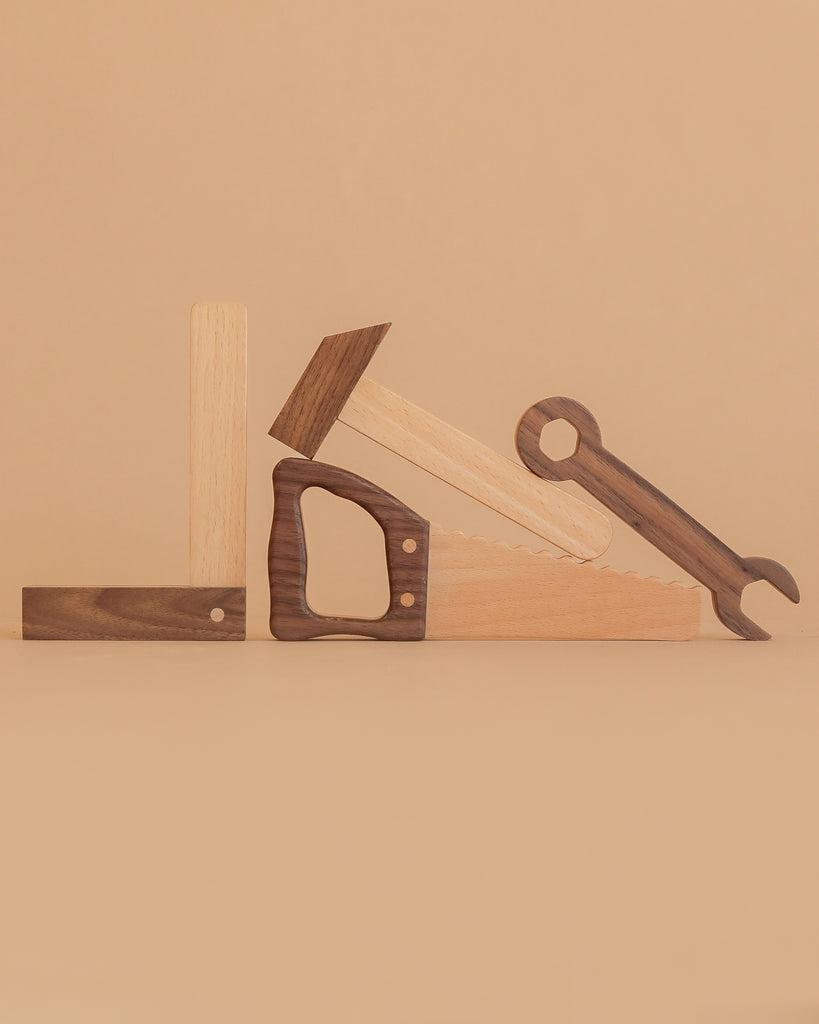 The Wooden Tool Set features a square, hammer, saw, and wrench made of solid rubber wood, artfully arranged upright against a beige background so their shapes spell out “LOVE.”.