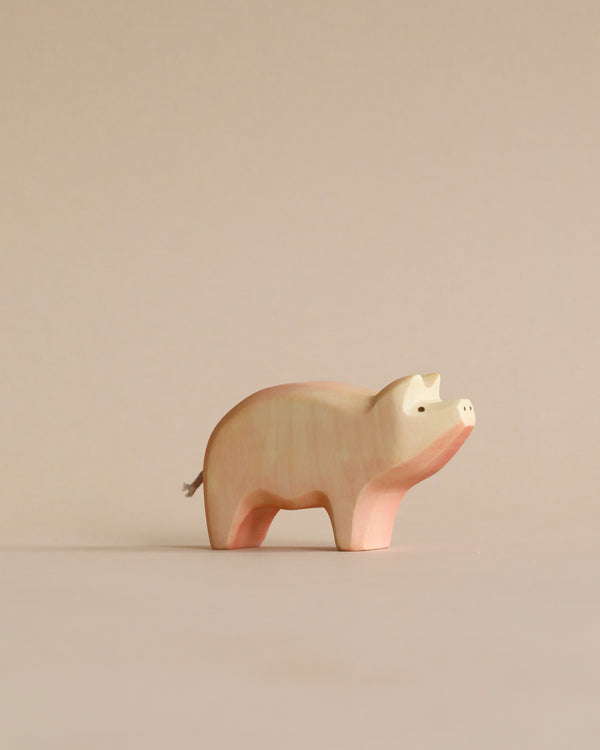 A Handmade Holzwald Pig, crafted with a smooth finish, displaying light pink and beige hues, standing against a neutral beige background. Suitable as part of educational toys collections.