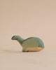 A high-quality, handmade Handmade Holzwald Whale toy, painted in shades of green and tan, on a plain beige background.