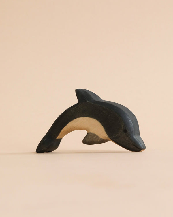A high-quality Handmade Holzwald Dolphin figurine with a smooth finish, displayed against a soft peach background. Its colors transition from dark blue to white, emphasizing its curved shape.