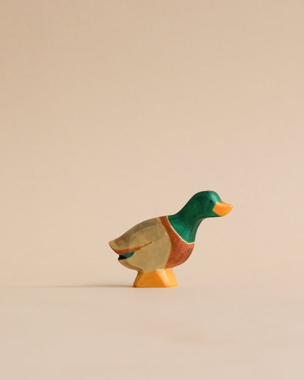 A colorful Handmade Holzwald Male Duck figurine, showcasing shades of green, orange, and beige, stands elegantly against a plain, light beige background. This high-quality wooden toy is both charming and durable.