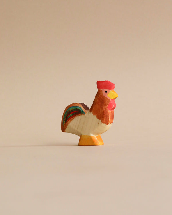 A small, colorful high-quality Handmade Holzwald Rooster figurine stands against a plain, light beige background, featuring painted details in red, white, and green.