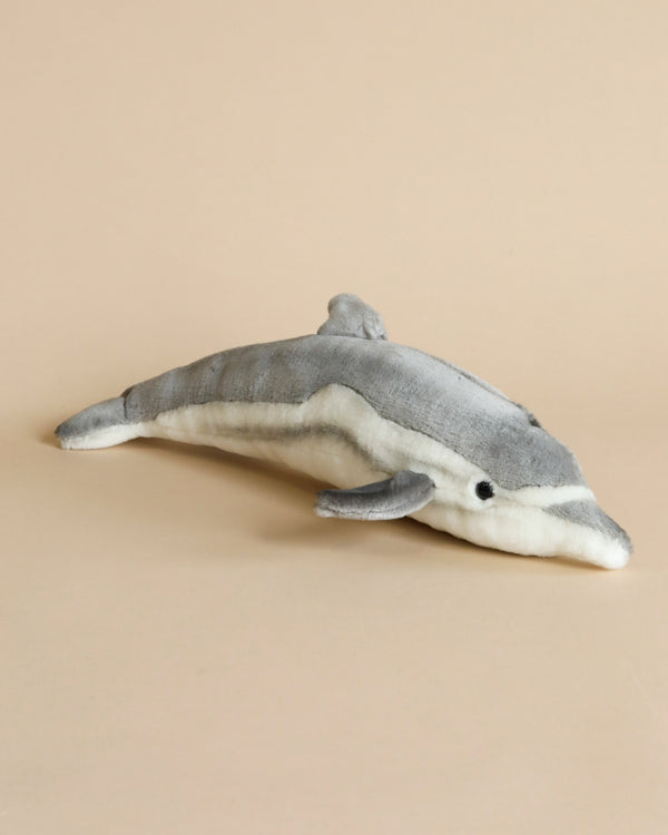 A Dolphin Stuffed Animal with realistic features and a soft gray and white color scheme, lying on a plain light beige background.