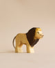 A Handmade Holzwald Lion figurine with a smooth, shining finish and painted details such as a mane, eyes, and whiskers, standing against a light beige background.