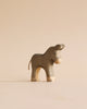 A small, wooden donkey figurine from the Handmade Holzwald Shepherd with Farm Animals Set features a minimalist design and stands on a beige surface against a matching beige background.