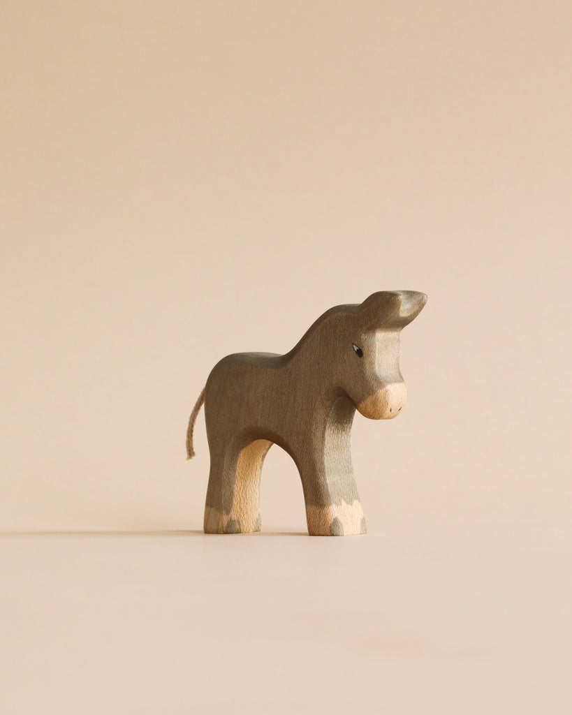 A small, wooden donkey figurine from the Handmade Holzwald Shepherd with Farm Animals Set features a minimalist design and stands on a beige surface against a matching beige background.