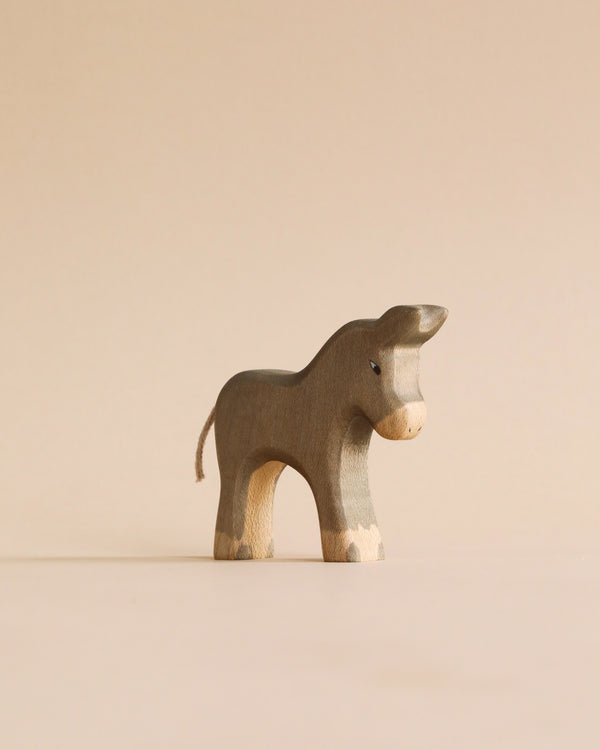 A Handmade Holzwald Small Donkey on a beige background, featuring a simplistic design with visible wood grain and painted details like eyes and nostrils, embodies the charm of sustainable toys.