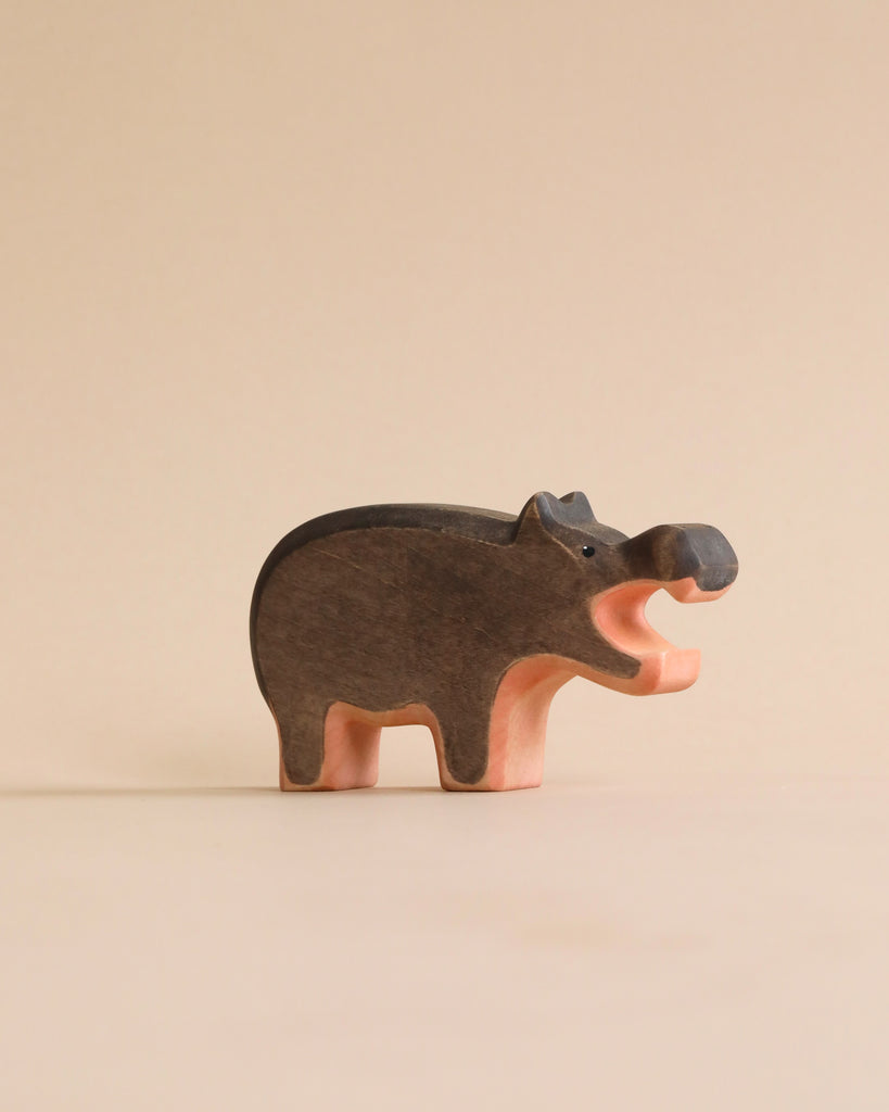 A Handmade Holzwald Hippo figurine with a smooth, dark brown back and a lighter pink underbelly stands against a plain beige background. This figure is part of our sustainable toys collection.