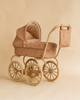 The Konges Sloejd Mini Doll Pram in Cherry Blush features a vintage design with large spoked wheels, cushioned pink fabric, a matching bag on the handle, and is shown against a beige background.