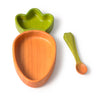 The Cathy the Carrot Plate & Spoon Set, featuring a wooden carrot-shaped bowl with a green leaf detail at the top and crafted from non-toxic Hevea wood, is displayed alongside its matching green wooden spoon on a white background.