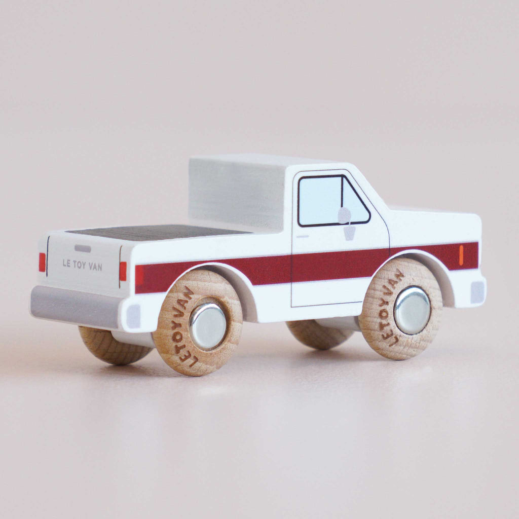 The No. 30 GT165 Charlie | Made in England is a classic toy truck crafted from white wood, accented with a bold red stripe and sturdy wooden wheels. Displayed from the back left side, it features “Le Toy Van” printed on both the wheels and tailgate, making this charming off-road vehicle perfect for imaginative play.