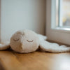 The Senger Naturwelt Cuddly Animal - Owl, a soft white plush toy with stitched eyes and beak, rests on a wooden floor by the window.