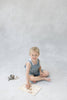 A young child with blonde hair sits on the floor, smiling, while playing with the Farm Animals Wooden Puzzle: A Tabitha Paige Puzzle, which features friendly animals. Several puzzle pieces are scattered nearby, making this engaging educational toy both fun and beneficial for toddlers. The background is light and neutral.