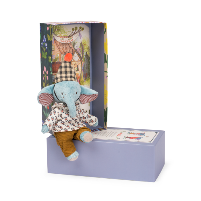 The Moulin Roty Pablo the Elephant - The Minouchkas sits in patterned clothes on a purple box, with a matching open case behind it that features vibrant floral designs and an illustrated house background.