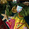 A close-up of a colorful Christmas stocking hanging on a garland with dried orange slices, a wooden snowflake ornament, and a Pollinator Seed Pop (Single)—a thoughtful gift for anyone dreaming of starting a pollinator garden.