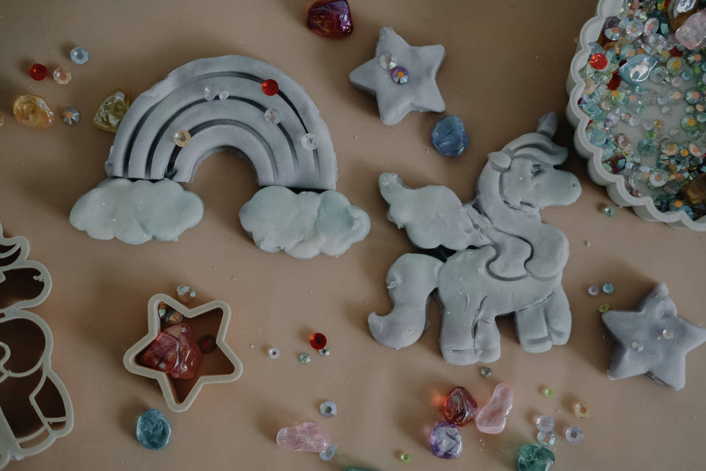 Craft charming clay figures of rainbows, clouds, and unicorns with the Unicorn Cutter Set - Eco Playdough Tool. Surround your creations with star-shaped objects, beads, and colorful gems scattered on a beige surface—perfect for inspiring sensory play.