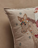 Close-up of the Christmas Donkey Pillow, featuring a beige surface with an embroidered donkey's head adorned with colorful flowers and stars, set amid festive holiday decor; part of a red and white outfit appears on the right.