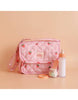 The Tiny Nurturers Set - Strawberry Picnic For Dolls, featuring a pink quilted doll nappy bag adorned with strawberries, a baby bottle, spoon, jar of magic baby doll cereal, and a peach-colored ring, is arranged neatly against a matching peach background.