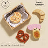 The Bakery & Patisserie Wooden Market Crate includes four pretend pastries—a palmier, croissant, pretzel, and iced bun—displayed in a wooden crate lined with newspaper print. Text: "7 Piece Set," "Crate & Newspaper Included," and "Hand Made with Love.