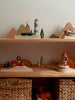 Two wooden shelves display colorful wooden toys, including the Sabo Concept Sea Adventure Set with a lighthouse, boat, bird, rainbow car, rocket, trees, woven baskets, and wooden blocks.
