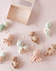 A hand-knit Cuddle + Kind Baby Sea Turtle (Kelp Green) lies on a pale pink surface decorated with small shell-shaped accents, alongside other baby animals and an open decorative box at the top.