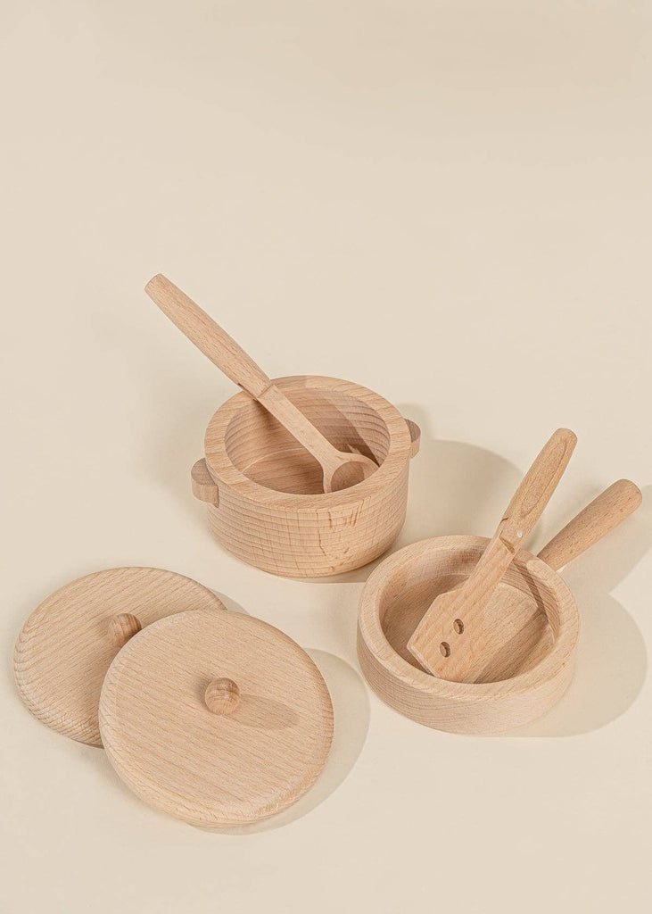 Two small wooden pots from the Wooden Pots and Pans Playset (6 Pcs), along with their lids, a wooden spoon, and a spatula, are arranged on a light beige surface. The lids rest beside the pots, creating a delightful display ideal for any children's wooden play kitchen or kids' cooking set.