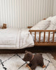 A cozy child's bedroom features a wooden bed with striped bedding, a small teddy bear on the bed, and the Pull-Along Raoul toy placed on a white rug with black lines. The wall has light vertical stripes.