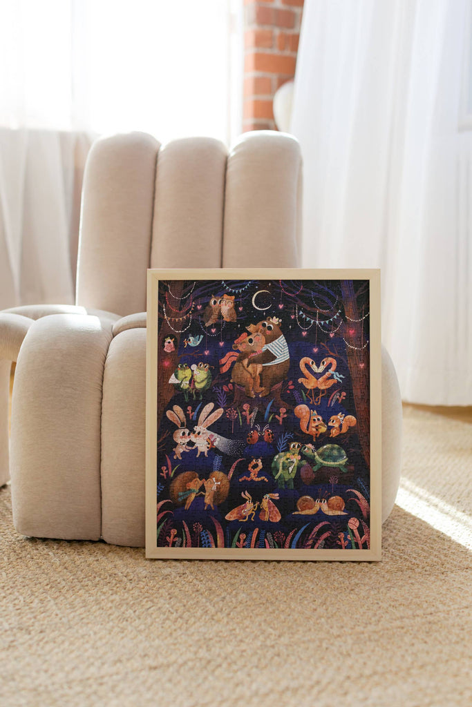 Bring home enchanting charm with the Courting Critters 500 Piece Puzzle, featuring a whimsical framed illustration of bears, rabbits, and foxes gathered beneath a crescent moon. Leaning against a plush beige chair on a carpeted floor in a softly lit room, this delightful scene makes the perfect inspiration for puzzling fun or serves as a thoughtful Valentine’s Day gift for someone special.