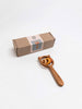 The Sabo Concept Bear and Rings Rattle - Yellow and Pink, shaped like a cat's head with circular rings inside, is shown beside a small labeled rectangular box on a white background, designed to help develop motor skills.