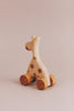 The Handmade Wooden Mini Giraffe Push Toy features a smooth finish and charming spotted details, mounted on four round wheels. It stands gracefully against a plain, neutral background.