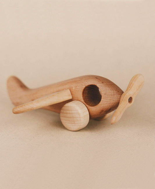 Handmade Wooden Airplane with a minimalist style and sleek finish, showcasing two circular wheels, a carved cockpit, and rounded wings. The natural linseed oil adds to its appeal against the beige background.