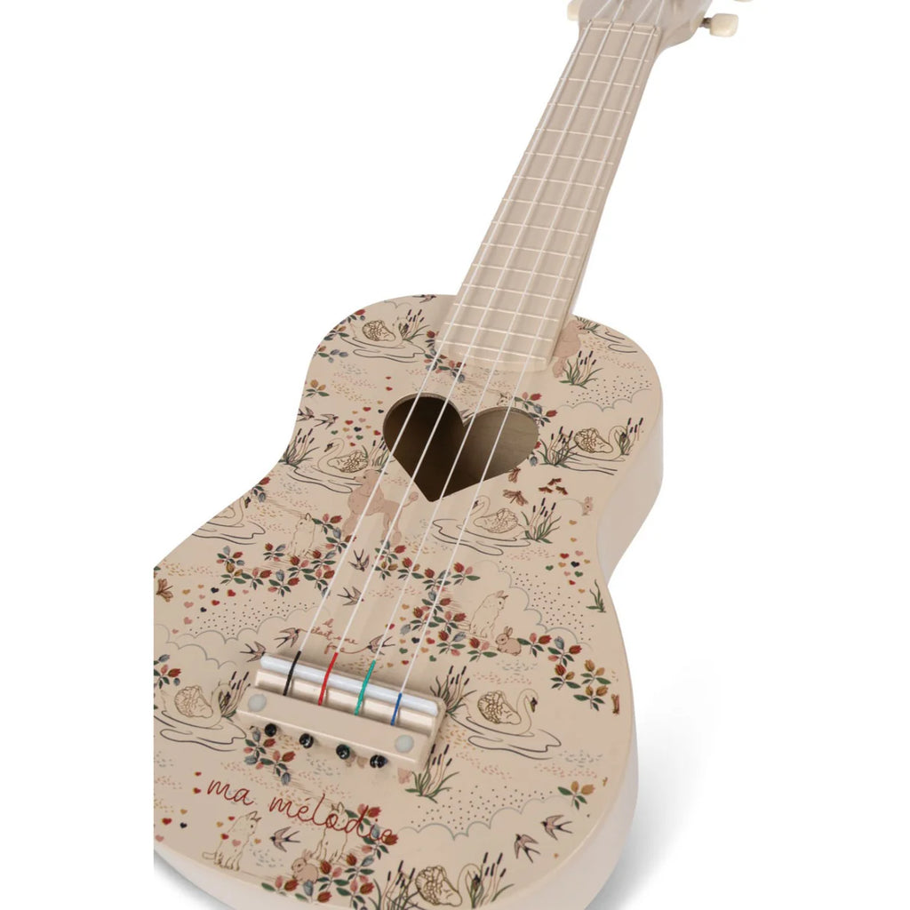 The Konges Sløjd - Wooden Ukulele - Mizumi, designed in a beige FSC-certified wood, features a heart-shaped sound hole and is adorned with intricate floral patterns, including swans and leaves. The inscription "ma mélodie" adds a personal touch, while colored markings on the strings bridge enhance its visual appeal, making this ukulele both an acoustic gem and an artistic masterpiece.