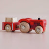 A red vintage wooden tractor labeled “No. 34 GT190 Tilly | Made in England” pulls a matching trailer carrying a small wooden block, perfect for imaginative play. Both feature natural wood wheels with visible text, set against a plain light background.