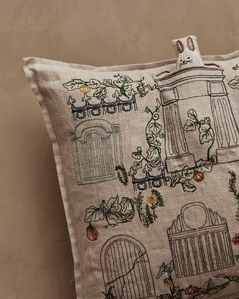 The Coral & Tusk Graveyard Pocket Pillow features beige fabric with embroidered gates, tombstones, and vines. A Bunny Ghost face tab adds whimsical charm to this cemetery-themed Halloween accent.