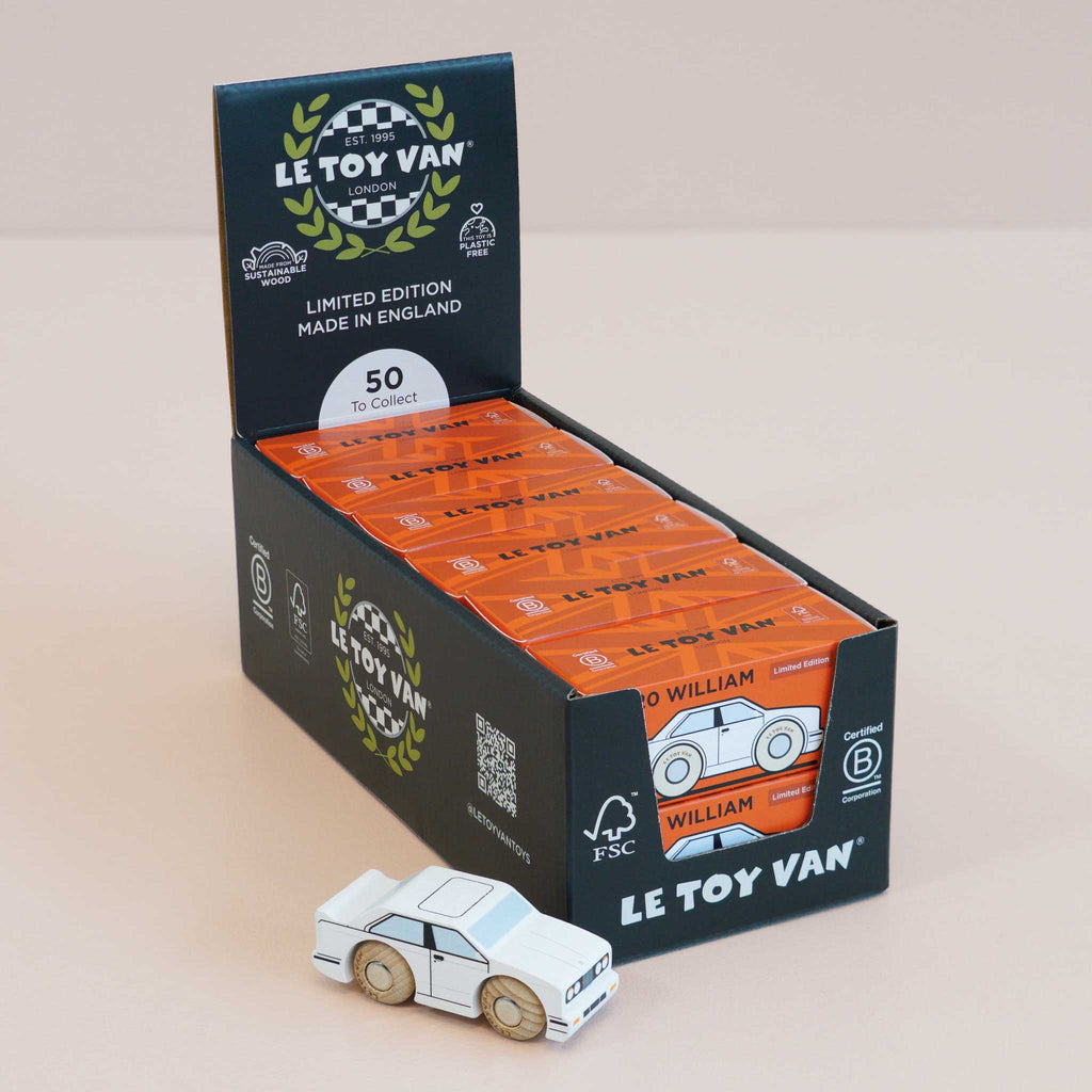 A display box holds several packages of the No. 21 GT120 William | Made in England toy car by Le Toy Van, each labeled “Limited Edition Made in England.” In front of the box sits a small white wooden racing car with wooden wheels, capturing the nostalgic charm of a vintage toy automobile.