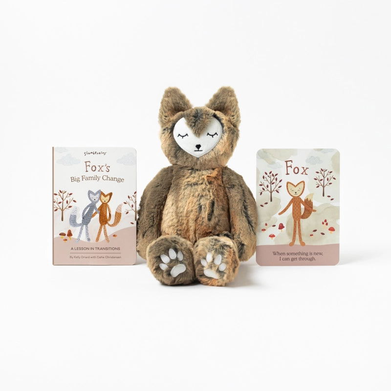 A Slumberkins Fox Kin + Lesson Book On Family Change, filled with hypoallergenic fiberfill, sits between two children's books titled "Fox's Big Family Change" and "Fox," against a white background. The toy features
