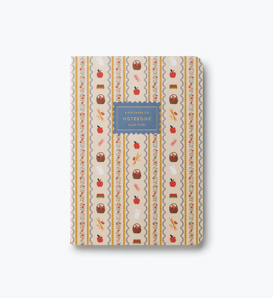 Introducing the Assorted Set of 3 Schoolhouse Notebooks—each with a patterned cover featuring apples, books, pencils, and paint tubes. A central label on a blue background reads “Ruled Paper 50s Notebook Ruled Paper.” These stitched notebooks offer convenient lay-flat binding for comfortable writing, making them ideal for all your classroom or creative needs.