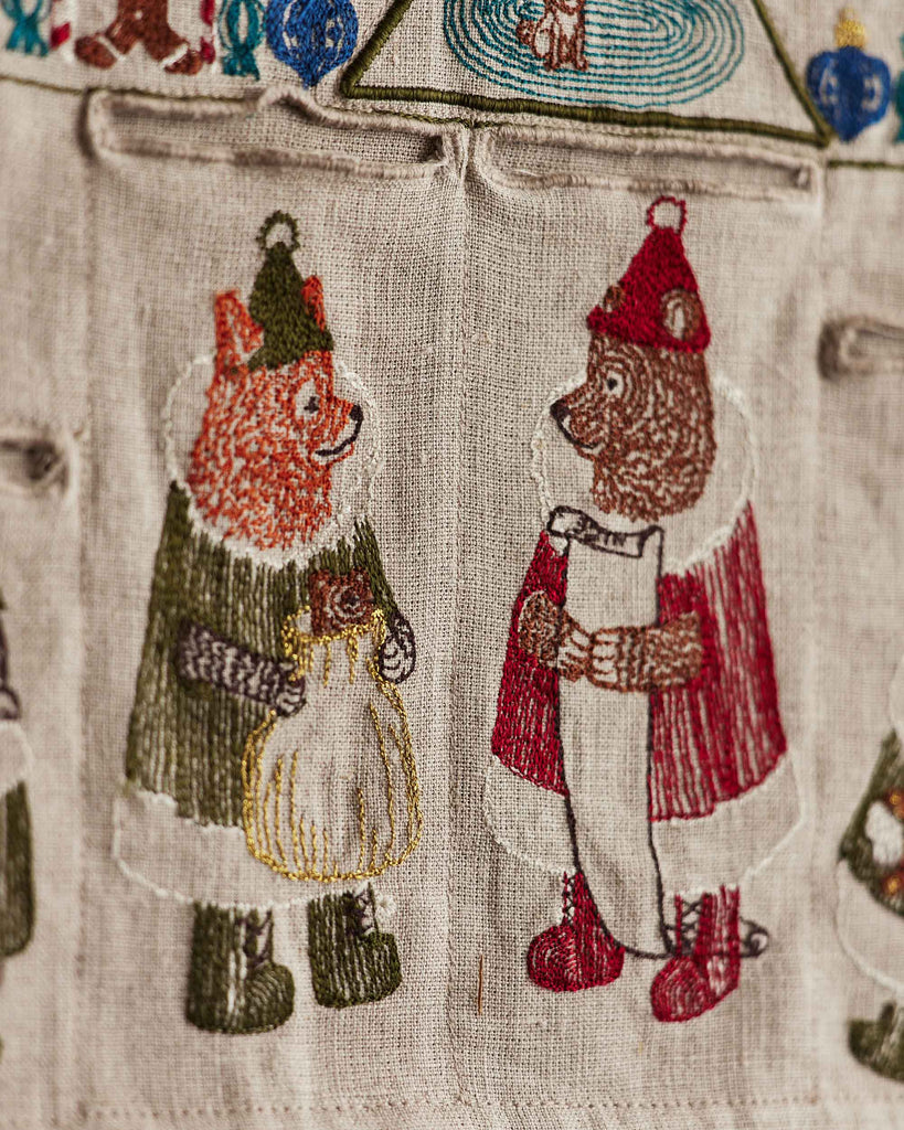 On the Coral & Tusk North Pole Advent Calendar, a fox in green with a sack and a bear in red with a scroll are embroidered facing each other on festive fabric for the Christmas countdown.