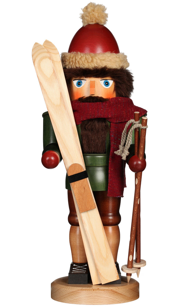 The Christian Ulbricht Collectible Wooden Nutcracker - Skier features a bushy brown beard, red hat with pom-pom, winter attire, red scarf, and holds skis and ski poles while standing on a round base.