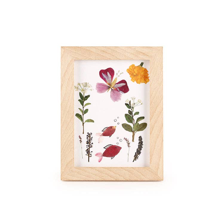 The Huckleberry Pressed Flower Frame features a beechwood frame displaying an illustration of flowers, leaves, and two small red fish swimming among the plants, with a yellow flower in the top right corner.