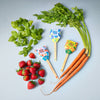 Fresh basil, strawberries, and carrots are arranged on a light blue background. Three seed packets—Sweet Basil, Giant Strawberry, Carrot Bunch—feature the family-friendly Garden Seed Pop (Single) with wooden plant markers.
