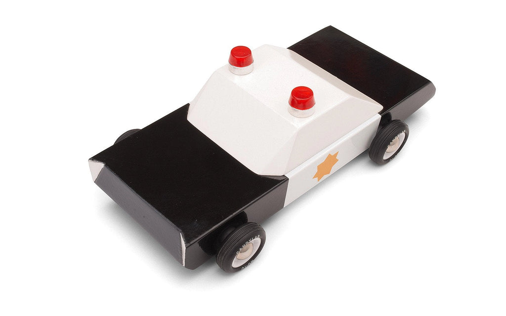 The Candylab Police Cruiser is a wooden toy police car expertly crafted from solid beech wood and painted in a sleek black and white design, complete with a gold star emblem on the side. It features two red lights on the roof and has four black rubber tires. Its simple, blocky design offers a timeless, classic look, and it has been safety tested for your peace of mind.