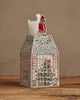 The Coral & Tusk Home for the Holidays Tissue Box Cover is a house-shaped, embroidered cover with brick walls, windows, a Christmas tree inside, and a red-clad figure on the roof, displayed on wood against a neutral background.