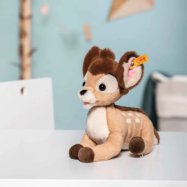 A Steiff, Disney's Bambi plush toy, 8 inches tall, with brown fur and white spots sits on a table, a price tag attached to its ear featuring the Steiff Button in Ear.