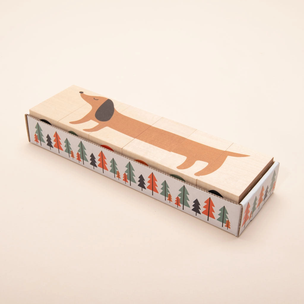 A rectangular box with a whimsical design featuring Uncle Goose Environments Neighborhood Blocks stretching along the length of the box, surrounded by a pattern of colorful basswood trees on the sides.