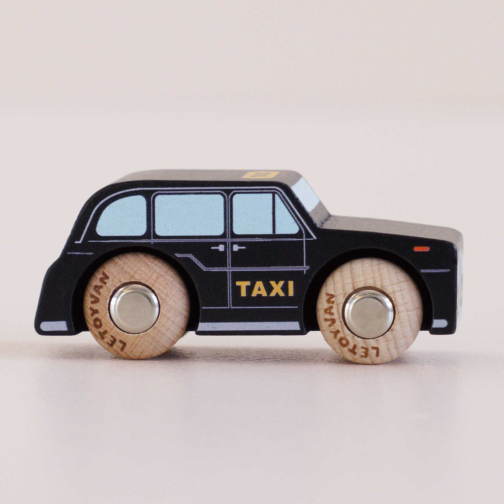 The No. 45 GT275 Bertie, made in England, is a black wooden taxi toy featuring “TAXI” on the side, light blue windows, and round wooden wheels—evoking the charm of a classic London car against a plain light background.