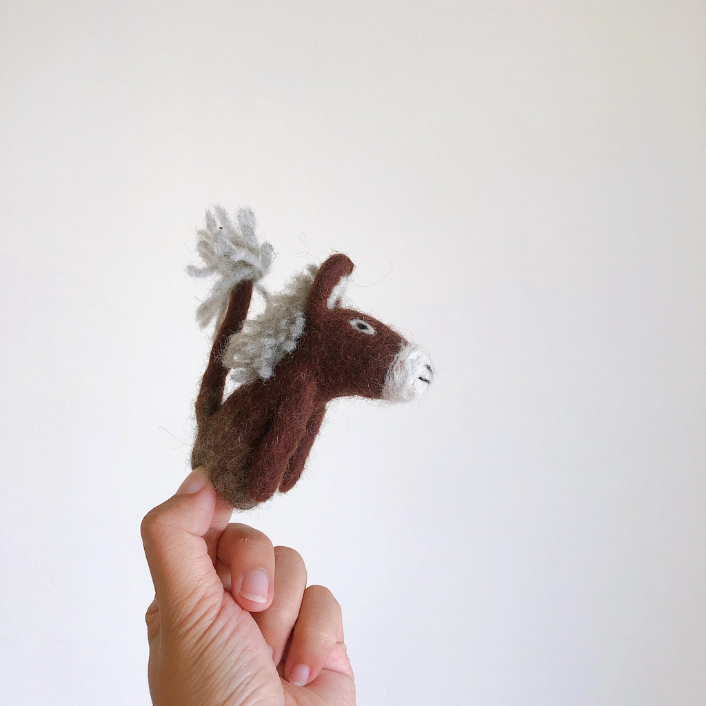 A hand displays the Felt Finger Puppet: Donkey, Brown—a handmade wool donkey with a white mane, perfect for storytelling—against a plain light background.