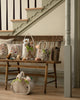 A rustic bench displays the Coral & Tusk Easter Parade Basket with spring accents. A bunny-shaped bag rests on the floor, adding charm and color to a hallway by the staircase.