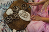 A child in a pink dress shapes white dough with the Pet Friends Faces Cutter Set – Eco Playdough Tool on a wooden board, surrounded by patterned fabric—creating a delightful scene of sensory play.