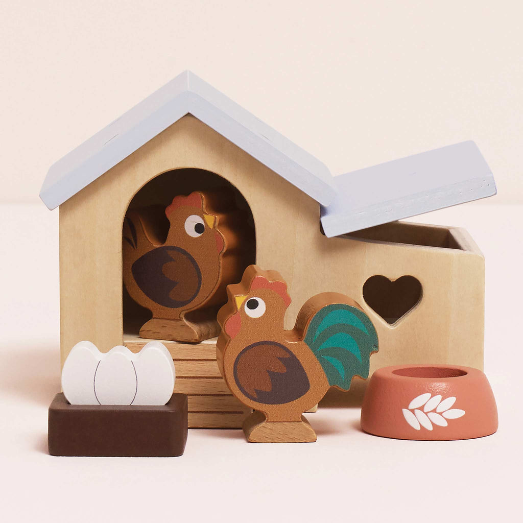The Chicken Coop Playset is a delightful farmyard toy with a hen house, 2 wooden chickens, 3 eggs, a nest, and red food bowl. Made from FSC-certified wood, it features a heart-shaped window and blue roof.
